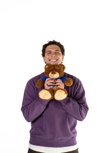 Luca  smiling while holding out a Bruno bear stuffed animal