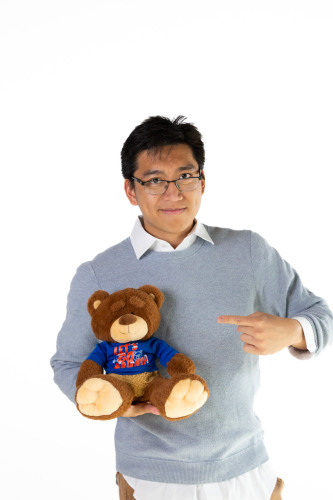 Avery posing with and pointing at a Bruno bear stuffed animal