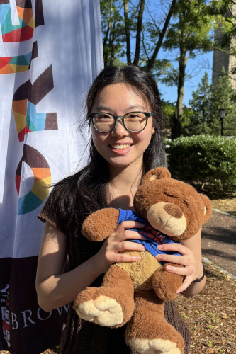 Alicia smiling outside in front of a New Student Orientation flag