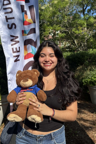 Alondra smiling outside in front of a New Student Orientation flag