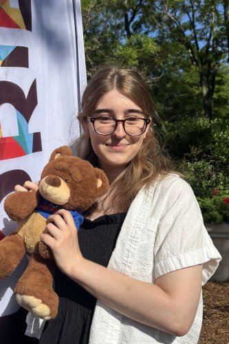 Charlotte smiling outside in front of a New Student Orientation flag