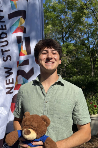Devan smiling outside in front of a New Student Orientation flag