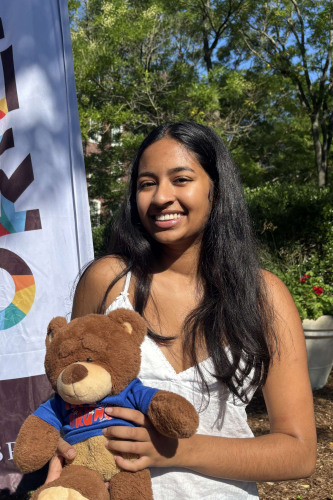 Diya smiling outside in front of a New Student Orientation flag