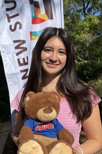 Grace smiling outside in front of a New Student Orientation flag