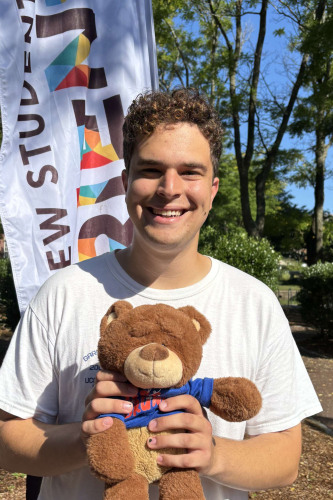 Ilan smiling outside in front of a New Student Orientation flag
