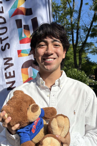 Keean smiling outside in front of a New Student Orientation flag