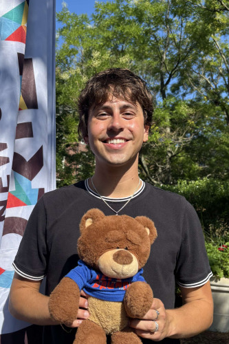 Remy smiling outside in front of a New Student Orientation flag