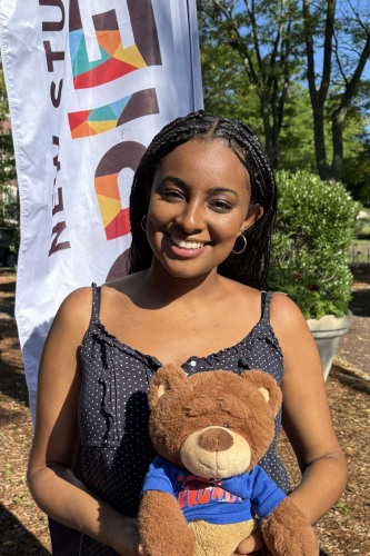 Soliyana smiling outside in front of a New Student Orientation flag