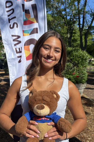 Sophie smiling outside in front of a New Student Orientation flag