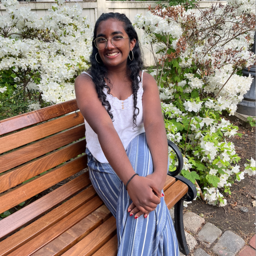 First Year Experience Fellow Vasu Jayanthi is sitting on a bench in a garden