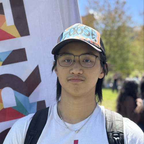 Alexander smiling outside in front of a New Student Orientation flag