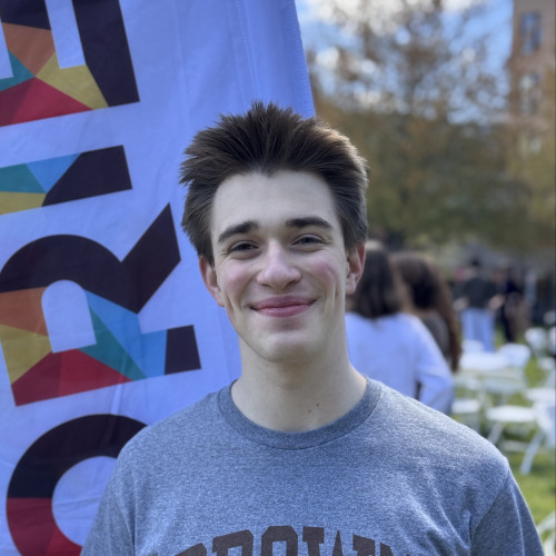 Charlie smiling outside in front of a New Student Orientation flag