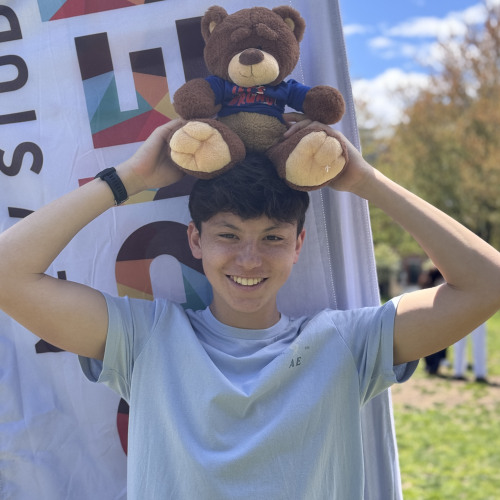 Emmitt smiling and posing with a Bruno stuffy outside in front of a New Student Orientation flag