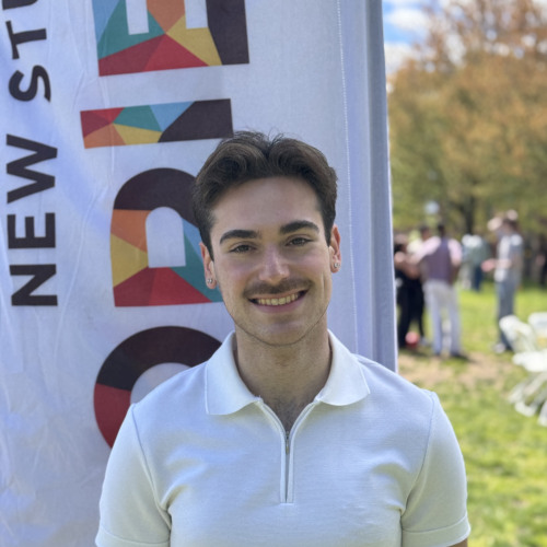 Hayden smiling outside in front of a New Student Orientation flag