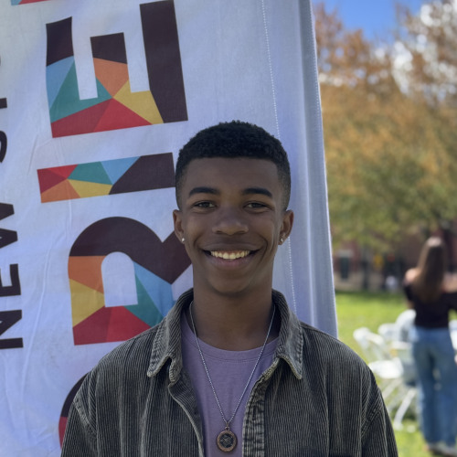 Jaiden smiling outside in front of a New Student Orientation flag