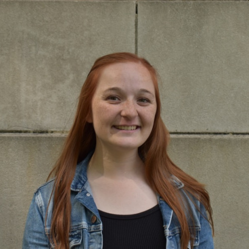 Female student infront of a cement wall smiling for photo