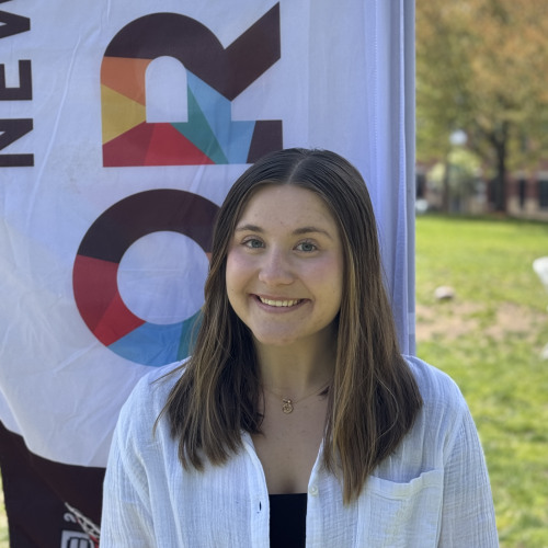 Lilly smiling outside in front of an orientation flag