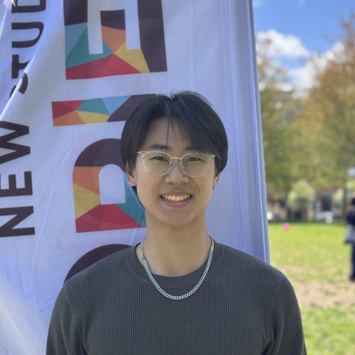 Minjun smiling outside in front of an orientation flag