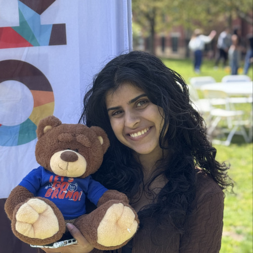 Mira posing with a bruno stuffy and smiling outside in front of an orientation flag