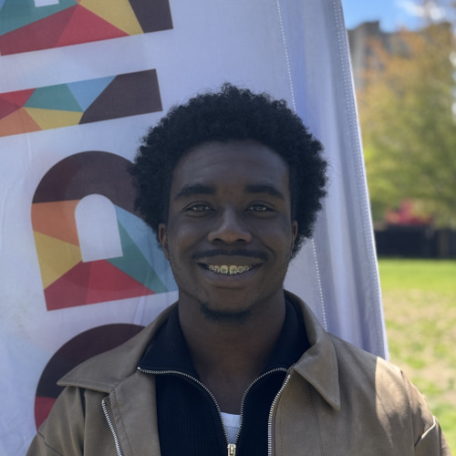 Ozochi smiling outside in front of an orientation flag
