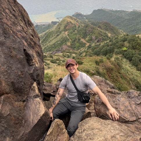 Student posing while climbing a mountain with mountains and ocean in background