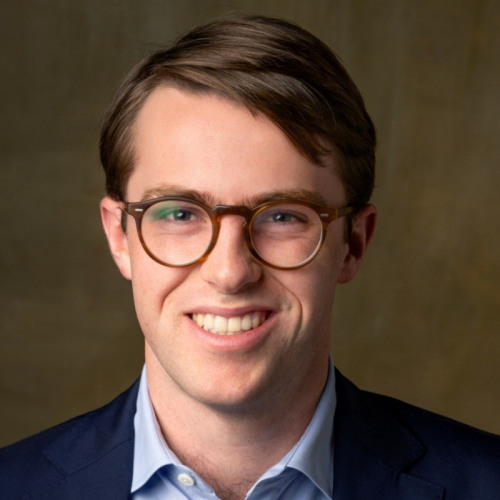 Professional headshot of student wearing business formal clothing and round glasses