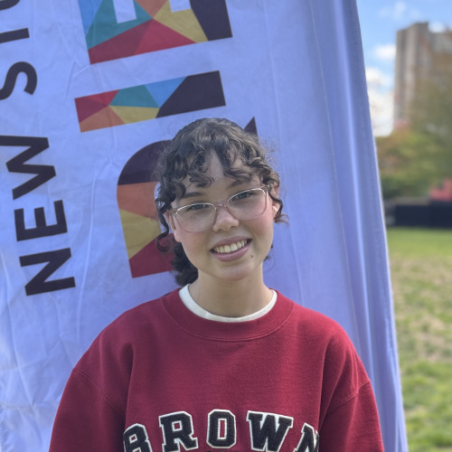 Avie smiling outside in front of a New Student Orientation flag