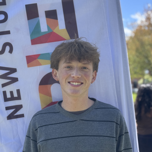 Jacob smiling outside in front of a New Student Orientation flag
