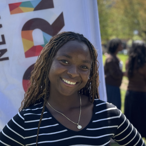 Layla smiling outside in front of a New Student Orientation flag
