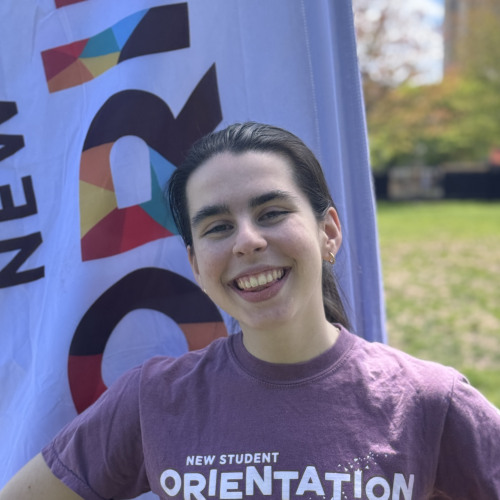 Cate smiling outside in front of an orientation flag