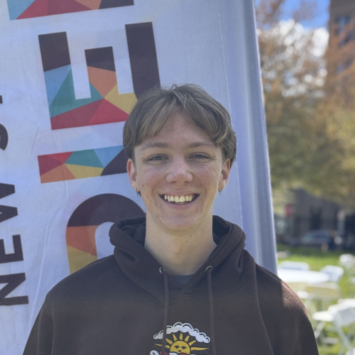 Andrew smiling outside in front of an orientation flag