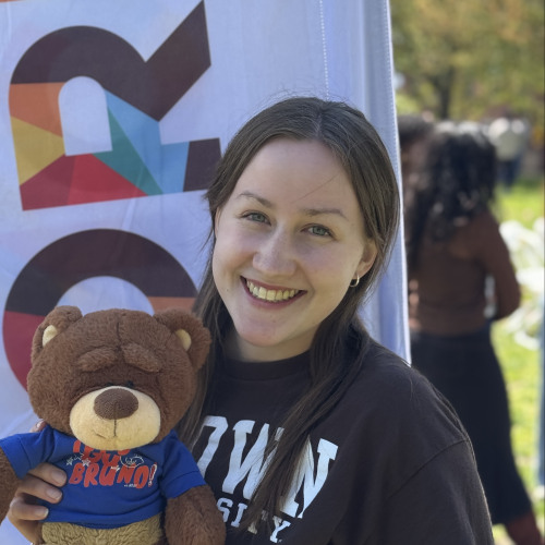 Verena posing with a bruno stuffy and smiling outside in front of an orientation flag