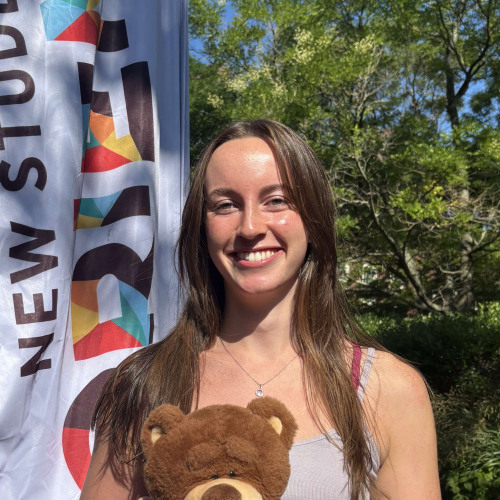 Abby smiling outside in front of a New Student Orientation flag