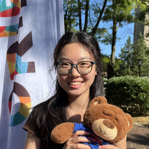 Alicia smiling outside in front of a New Student Orientation flag