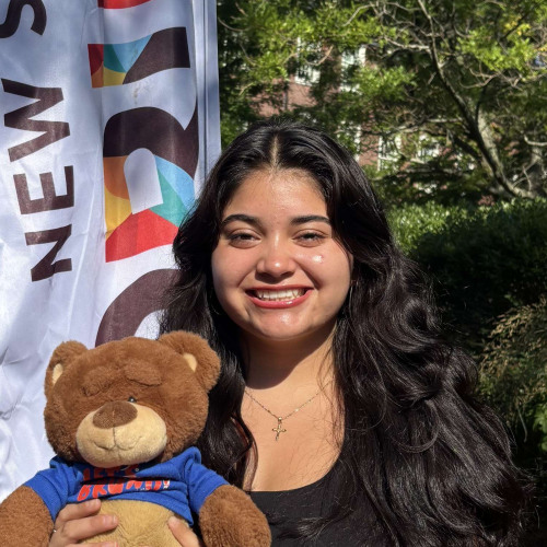 Alondra smiling outside in front of a New Student Orientation flag