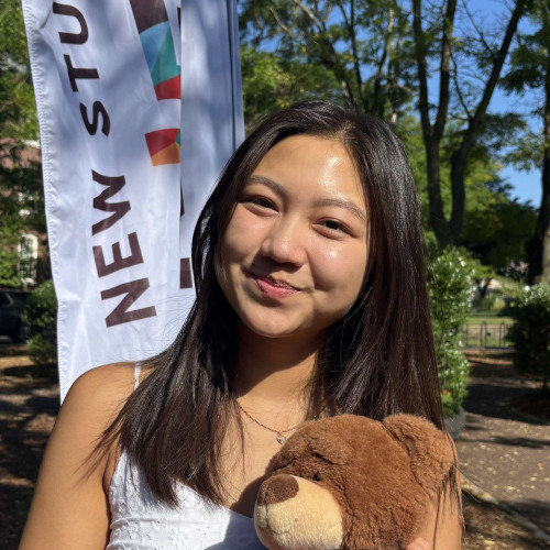 Amy smiling outside in front of a New Student Orientation flag