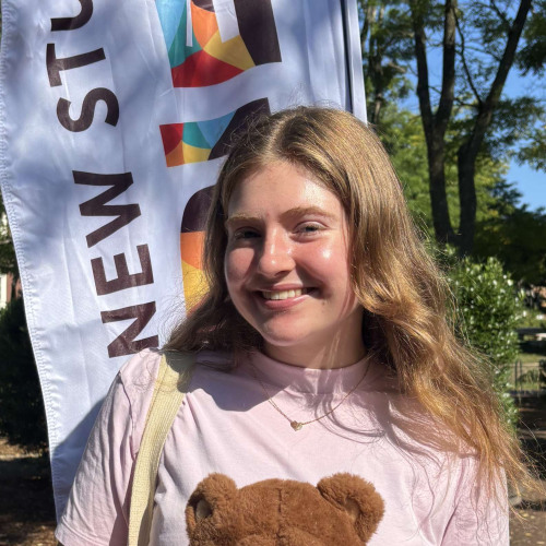 Audrey smiling outside in front of a New Student Orientation flag