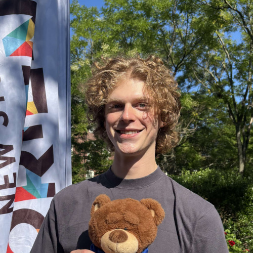 Ben smiling outside in front of a New Student Orientation flag