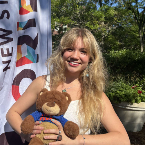 Camille smiling outside in front of a New Student Orientation flag