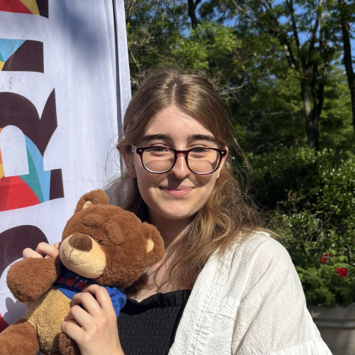 Charlotte smiling outside in front of a New Student Orientation flag
