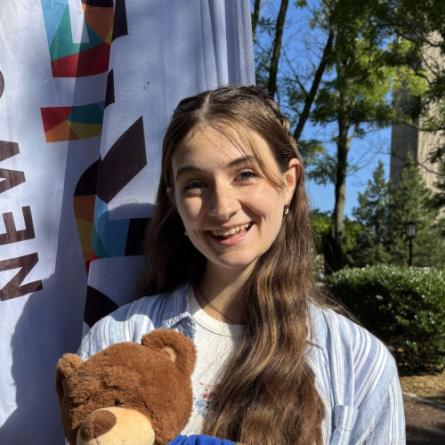 Corinne smiling outside in front of a New Student Orientation flag