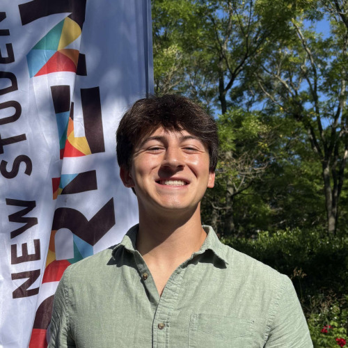 Devan smiling outside in front of a New Student Orientation flag