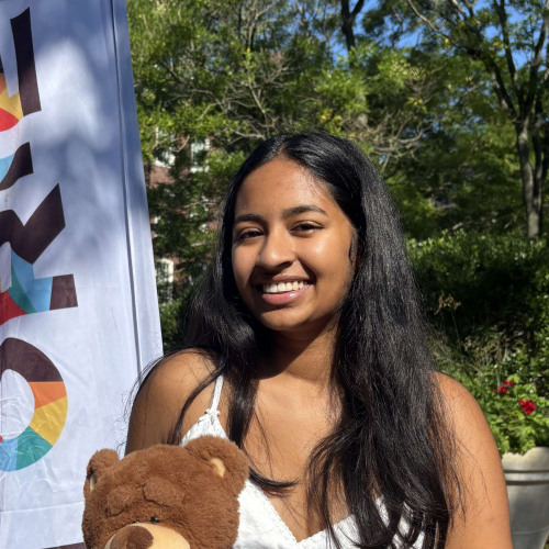 Diya smiling outside in front of a New Student Orientation flag