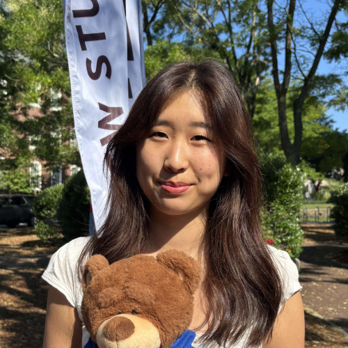 Elise smiling outside in front of a New Student Orientation flag