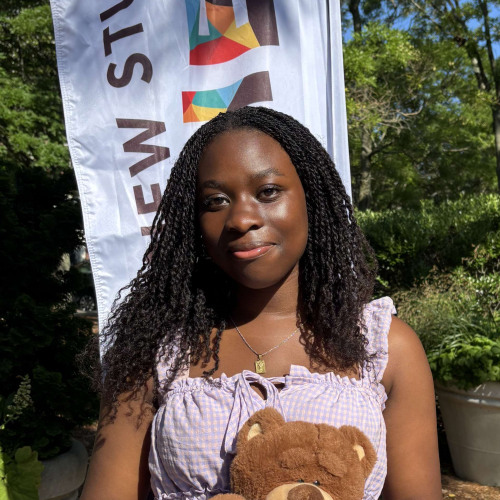 Faith smiling outside in front of a New Student Orientation flag