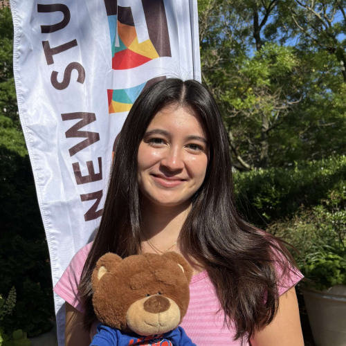 Grace smiling outside in front of a New Student Orientation flag