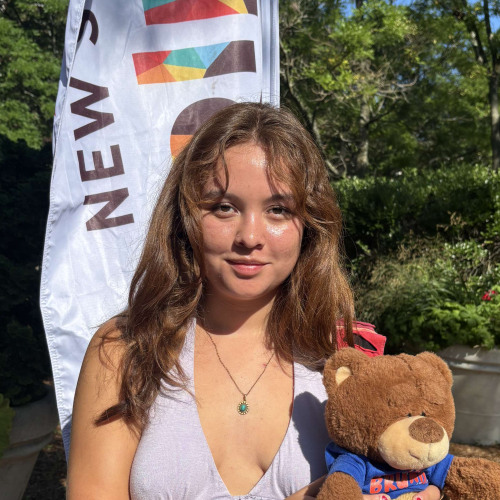 Graciela smiling outside in front of a New Student Orientation flag