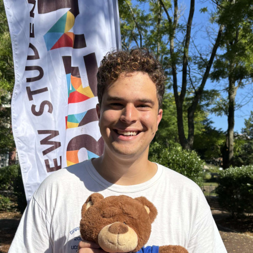 Ilan smiling outside in front of a New Student Orientation flag