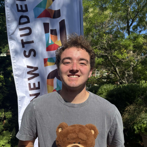 Jett smiling outside in front of a New Student Orientation flag