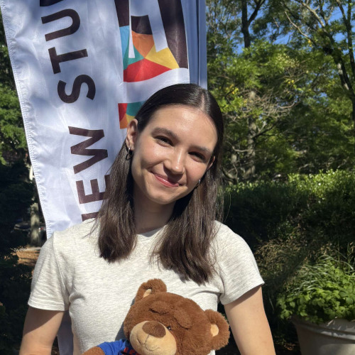 Kate smiling outside in front of a New Student Orientation flag